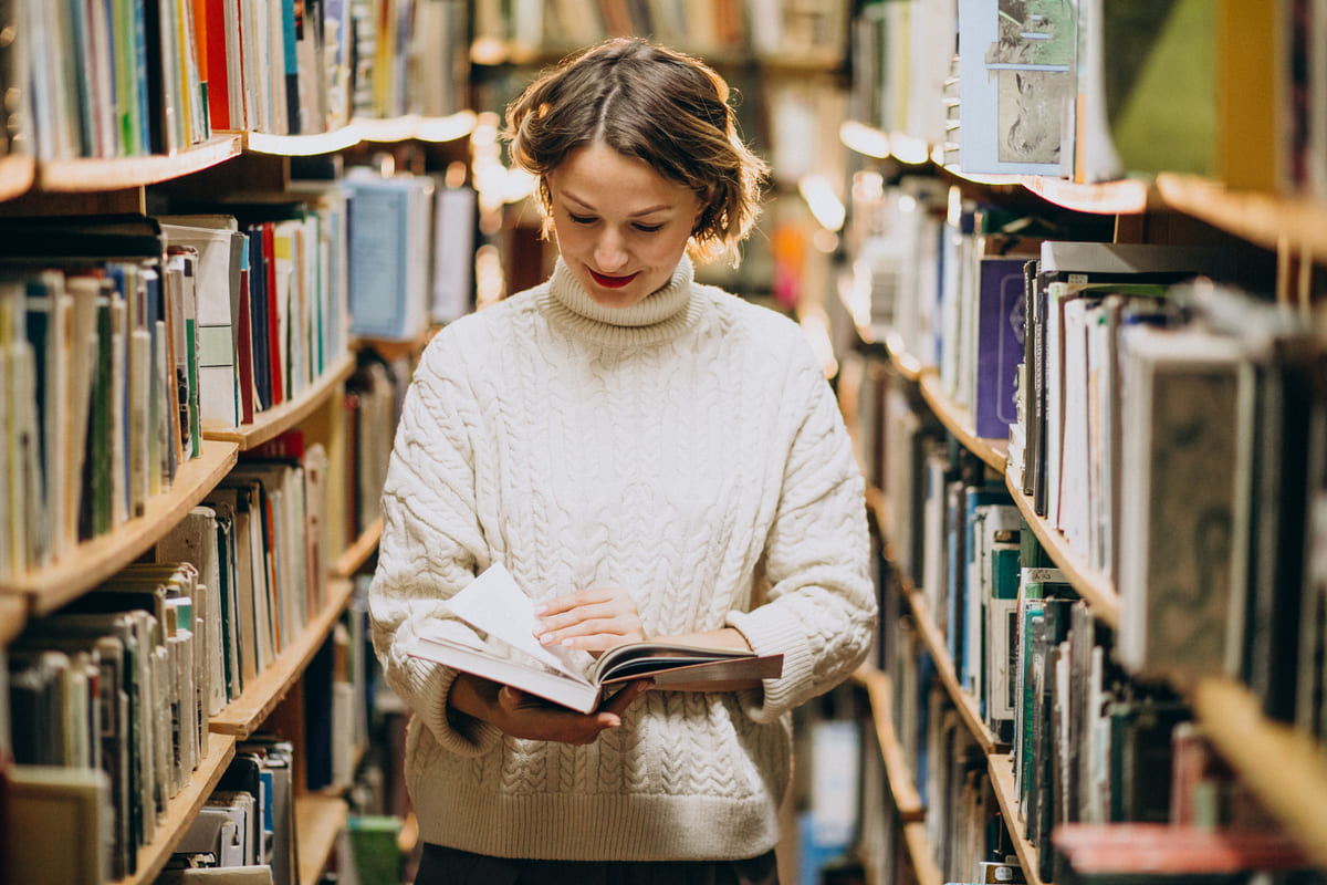 Uśmiechnięta czytelniczka z naręczem książek w bibliotece