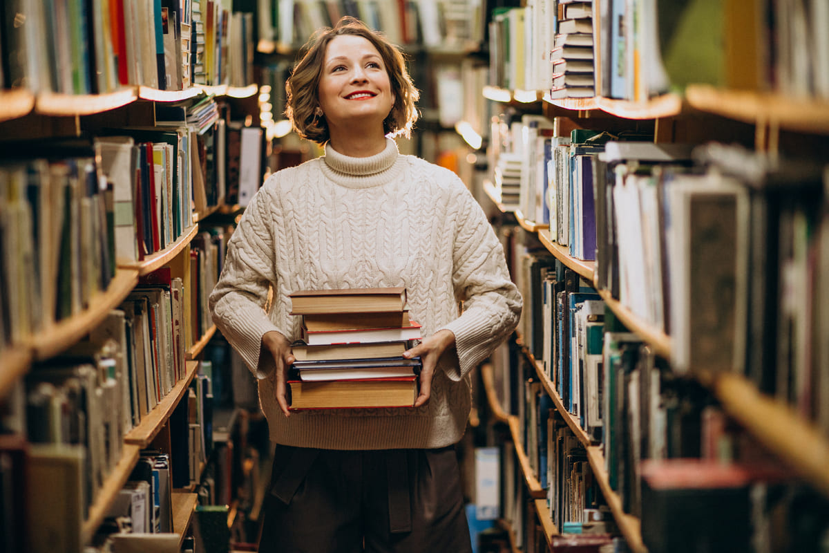 Czytelniczka przegląda książkę pomiędzy regałami biblioteki
